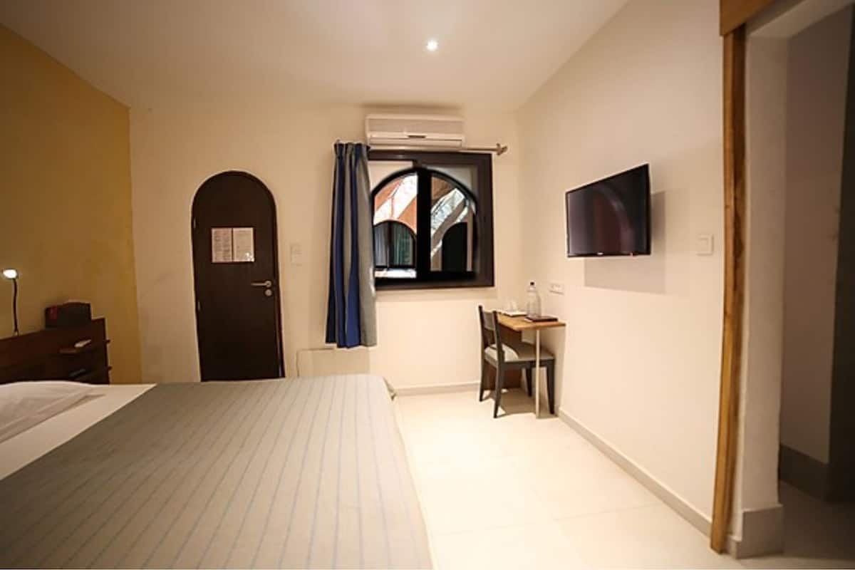 A hotel room with a bed, a desk, a chair, a TV mounted on the wall, and a window with curtains.