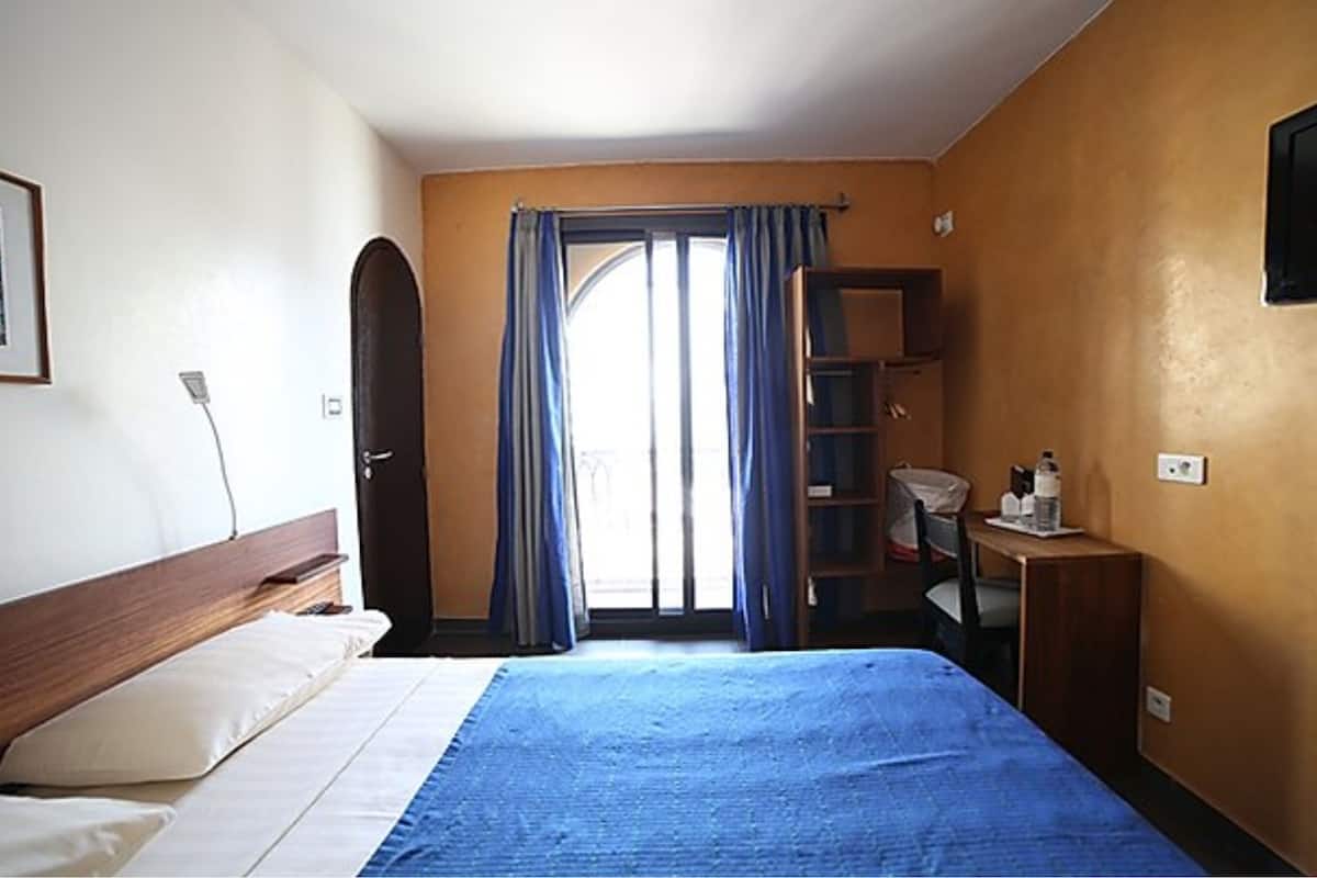 A hotel room with a bed, a desk, a chair, a wardrobe, and a television.
