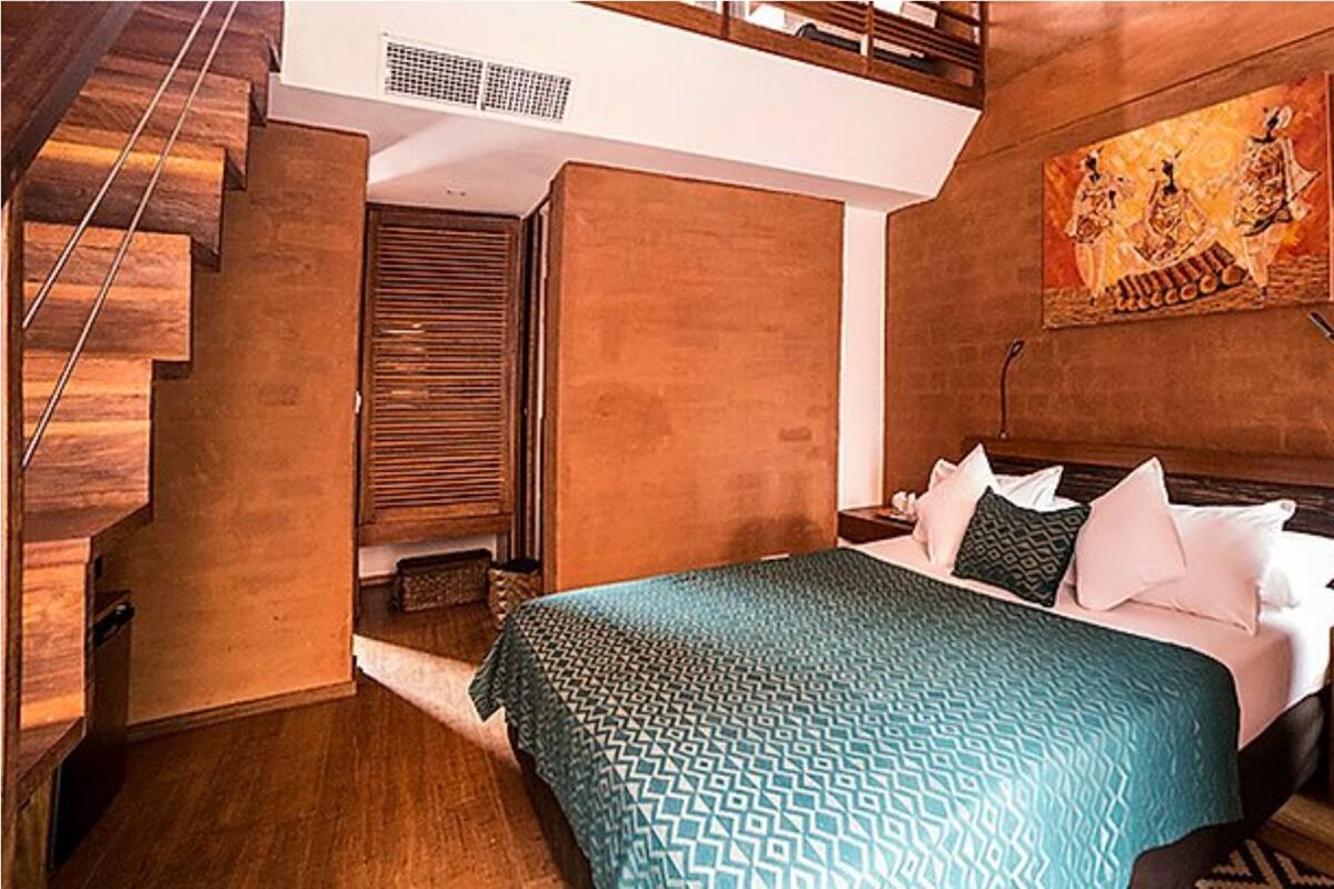 A bedroom with a bed, wooden walls, a staircase, and a painting.