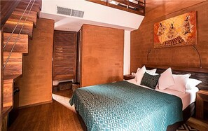 A bedroom with a bed, wooden walls, a staircase, and a painting.