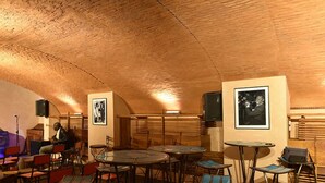 A cozy, rustic interior with wooden tables and chairs, a speaker, and framed pictures on the walls. - Hôtel Le Djoloff (Dakar)