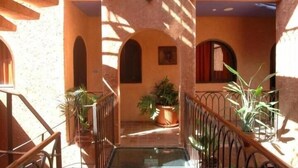 A sunlit corridor with arches, a glass railing, and potted plants. - Hôtel Le Djoloff (Dakar)