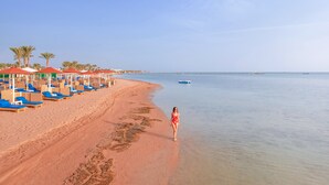 Une plage avec des transats et des parasols, un ciel dégagé et une mer calme.