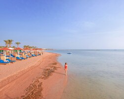 Una playa con tumbonas y sombrillas, cielo despejado y mar tranquilo.