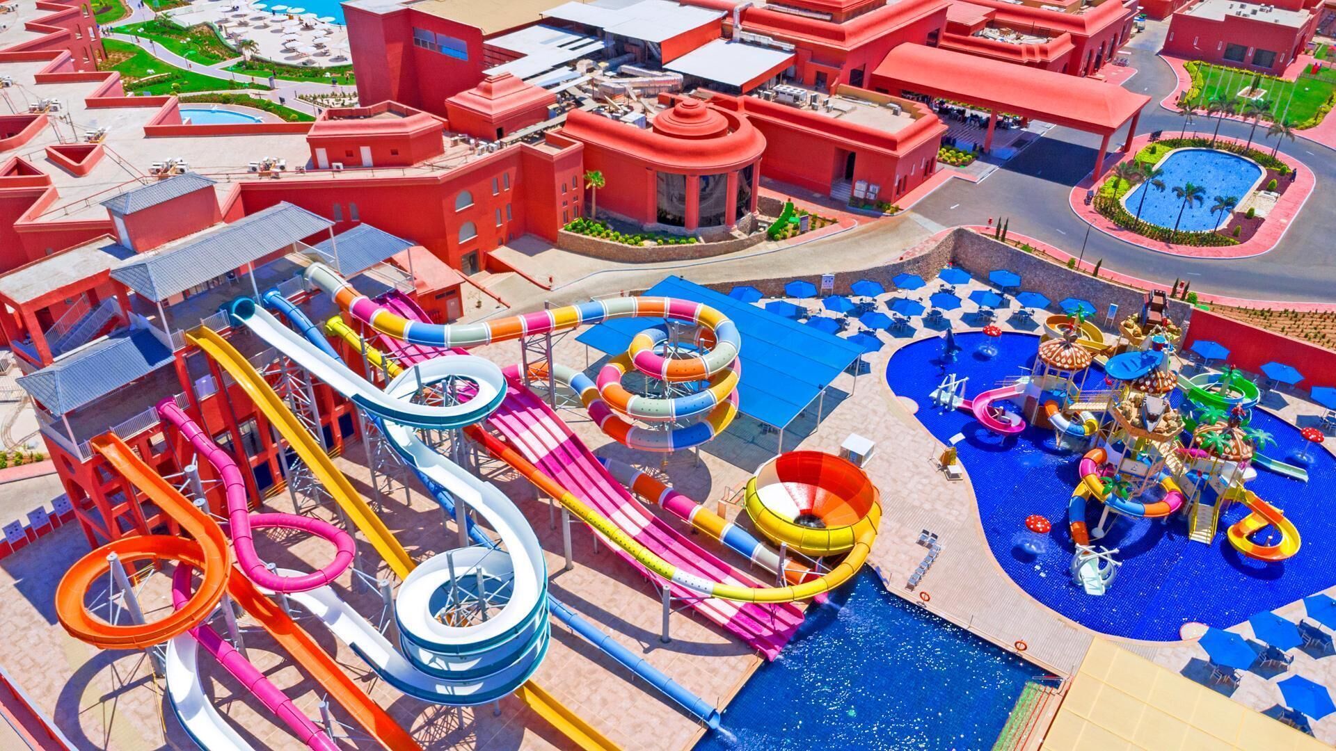 Un parc aquatique doté de nombreux toboggans et de plusieurs piscines, entouré de bâtiments rouges et d’un vaste espace dédié aux piscines.