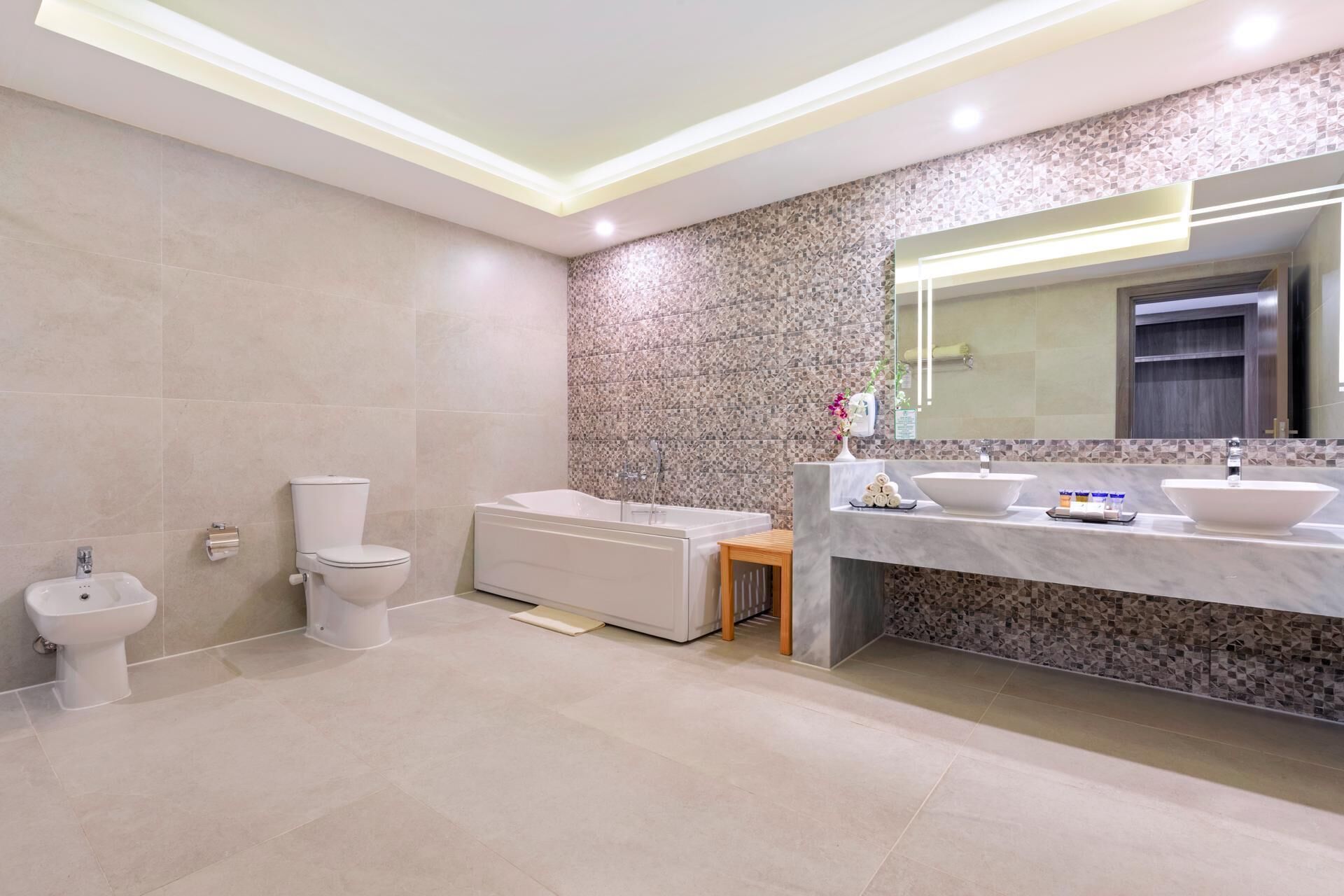 Un baño moderno con inodoro, bidé, bañera y tocador con dos lavamanos y un espejo.