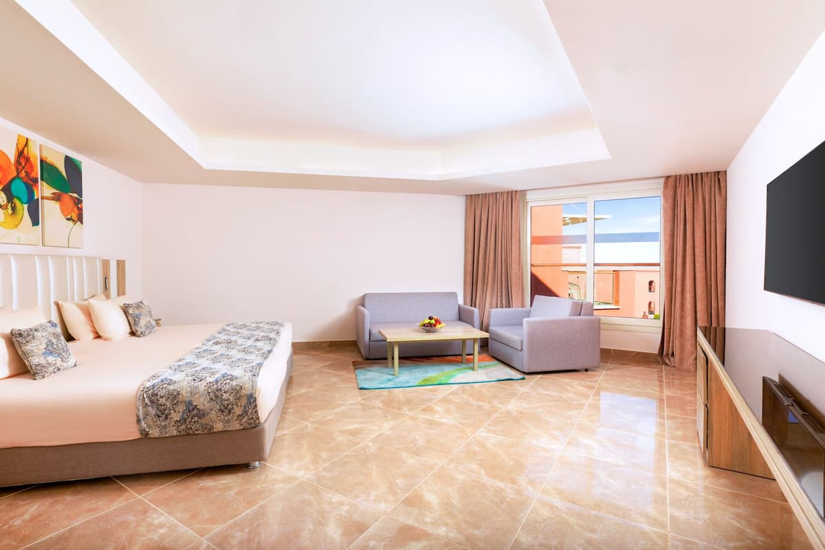 A modern hotel room with a bed, sofa, armchair, small table, and a TV.