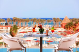 Una mesa con bebidas y un florero, con vista a una piscina y zona de playa.
