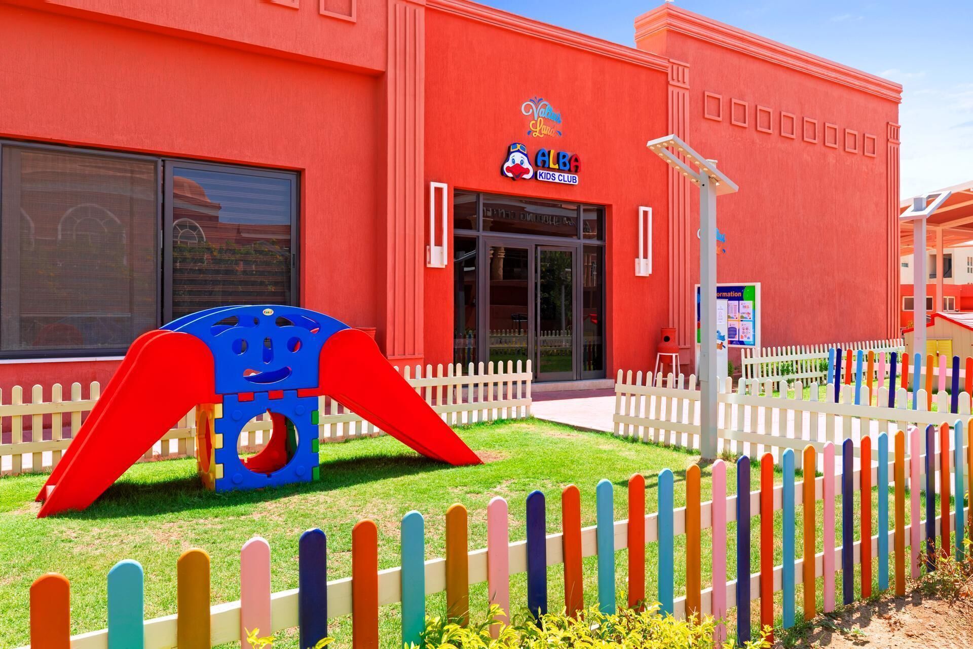 A red building with a sign for 'Valencia Plaza ALBA Kids Club'.