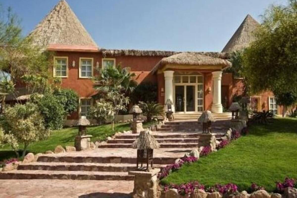 A building with a thatched roof, a central entrance with columns, and a stone staircase leading up to it.