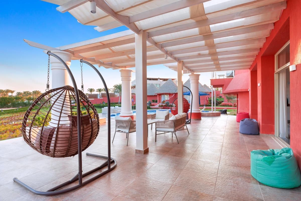 A covered outdoor area with a hanging chair, seating, and a pool.