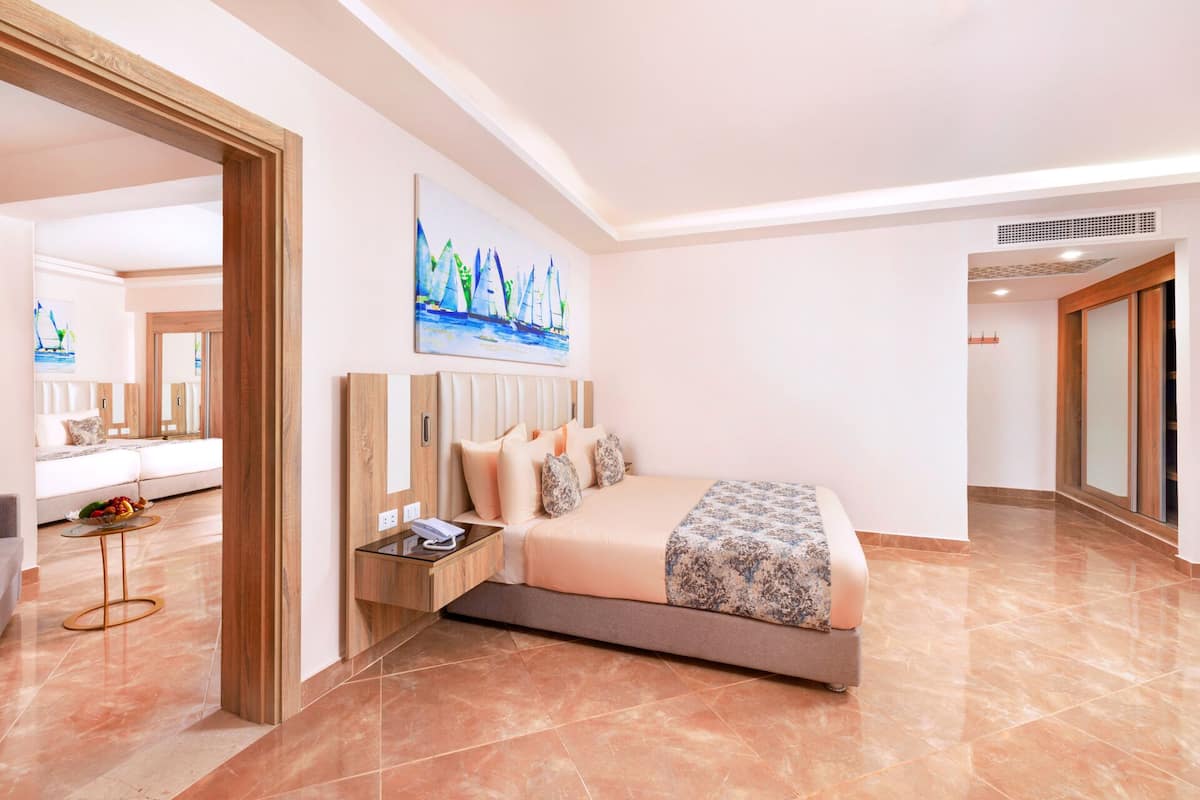 A modern hotel room with a large bed, a bedside table, a mirror, and a painting of sailboats on the wall.