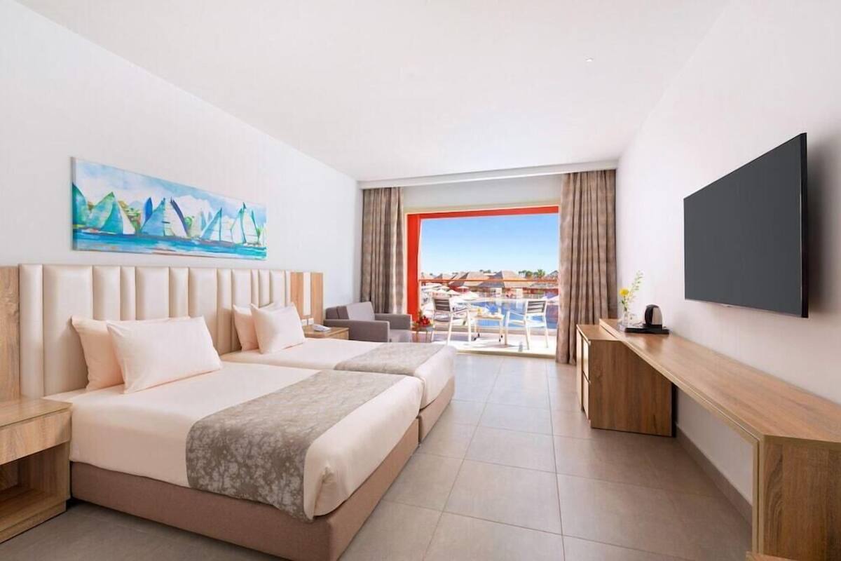 A hotel room with two beds, a TV, a painting, and a view of a swimming pool.
