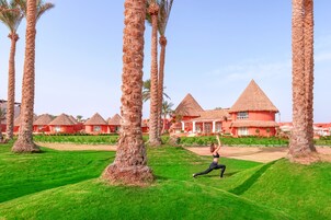 Un resort con edificios de techo de paja, palmeras y una persona realizando una postura de yoga.