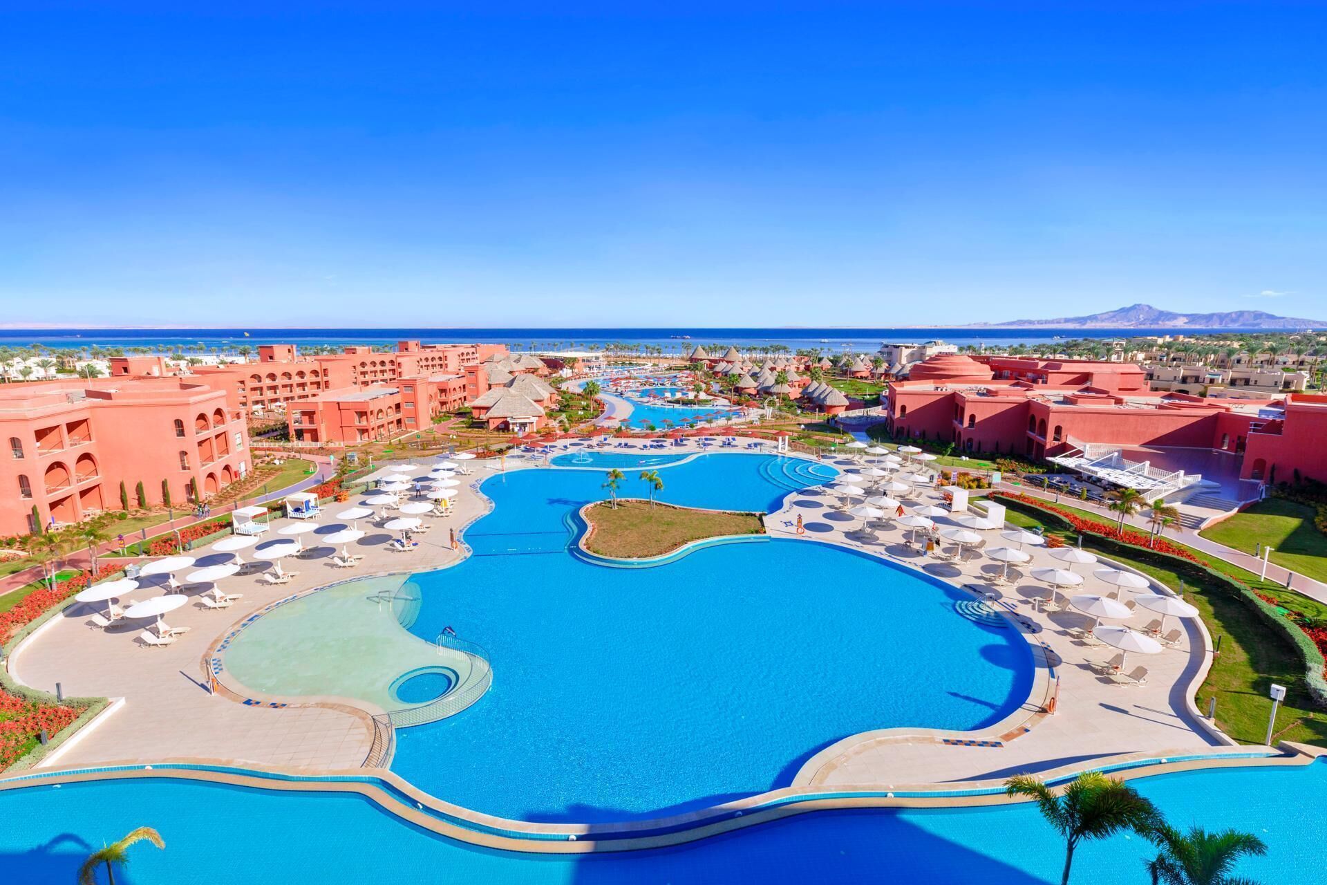 Een resort met diverse zwembaden, palmbomen en gebouwen met rode daken.