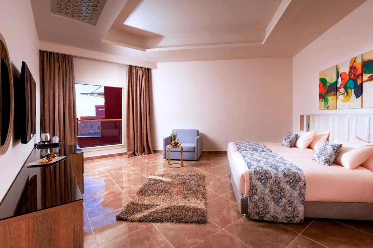 A hotel room with a bed, a sofa, a desk with a coffee maker, a chair, and a large window with curtains.