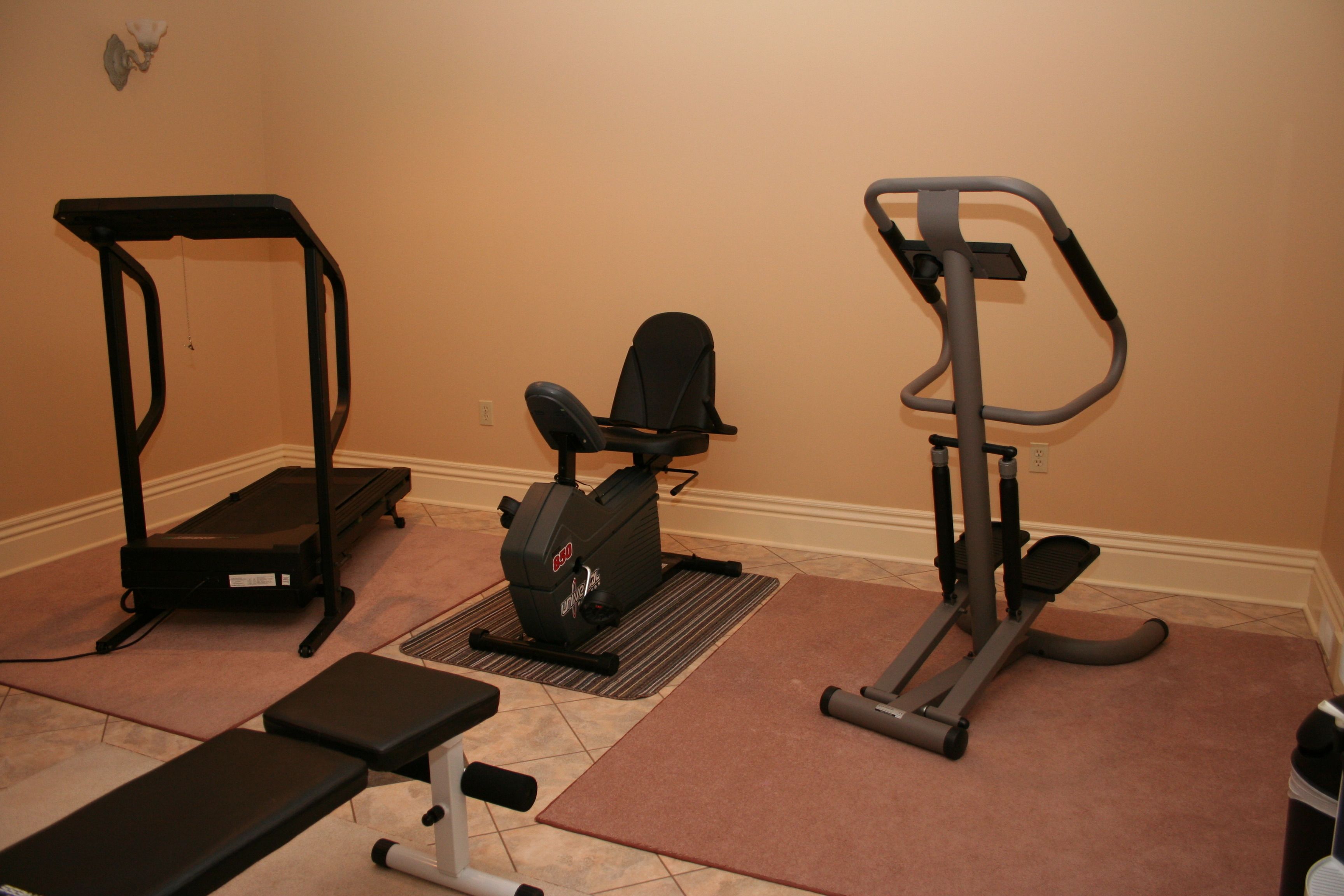 A home gym with a treadmill, elliptical, and bench.