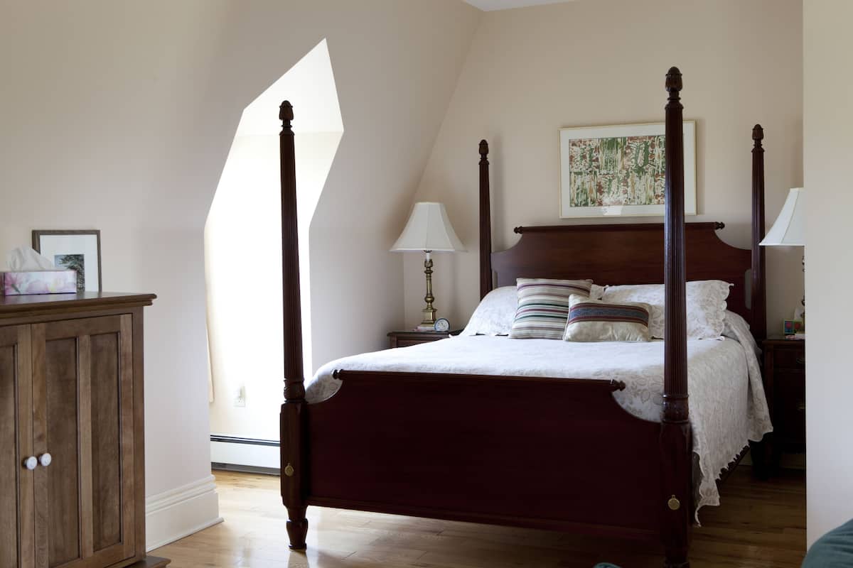 A four-poster bed with a wooden frame, a nightstand with a lamp, and a cabinet to the left.