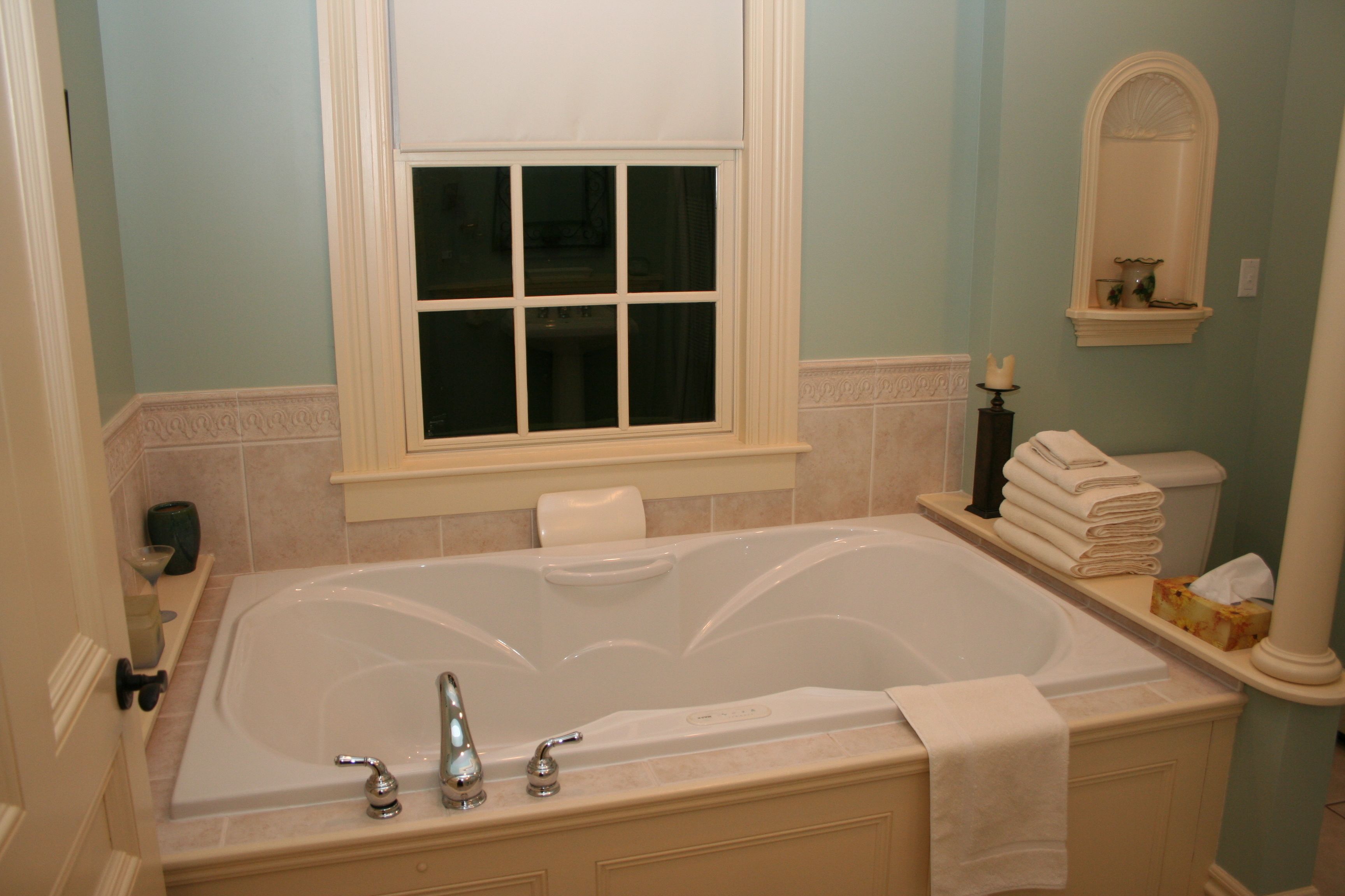 A bathroom with a large bathtub, a window, a mirror, and a towel rack.