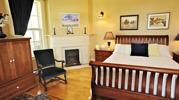 A bedroom with a wooden bed, a chair, a fireplace, and a nightstand with a lamp.
