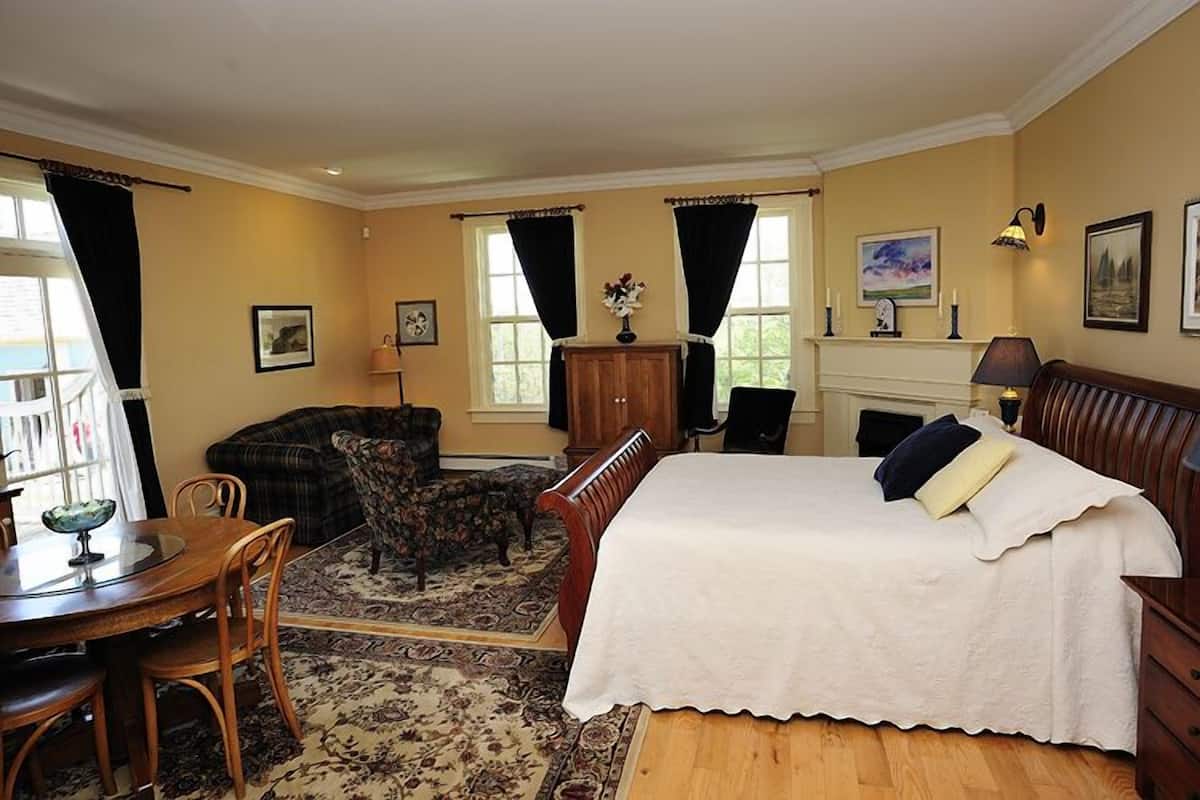 A room with a bed, a dining table with chairs, a sofa, and a fireplace.