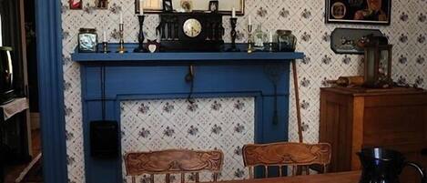 A dining area with a wooden table set with blue and white patterned tableware, a blue fireplace, and a wall-mounted clock.