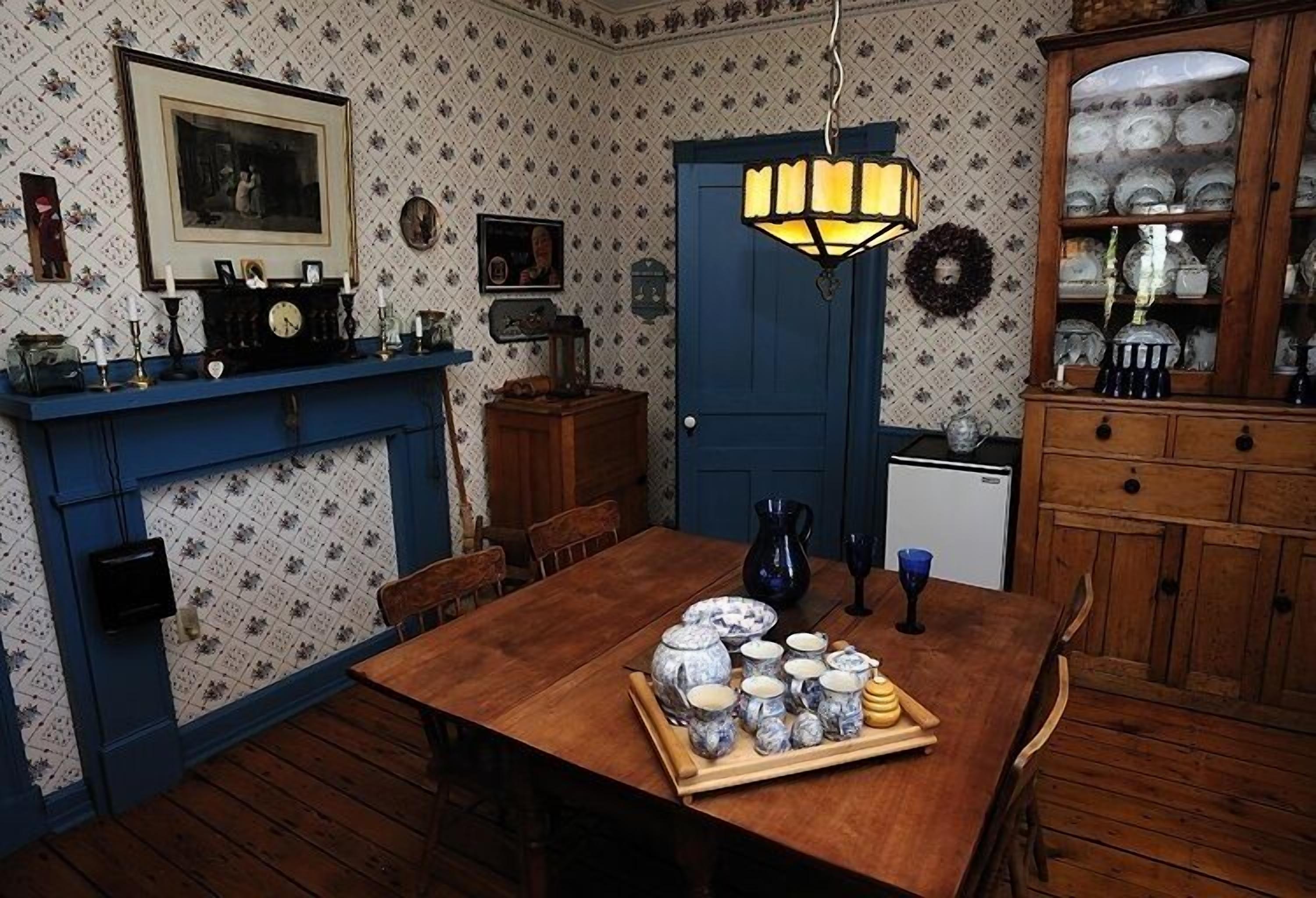 Une salle à manger avec une table en bois dressée pour le repas, une porte bleue et un buffet rempli de vaisselle.