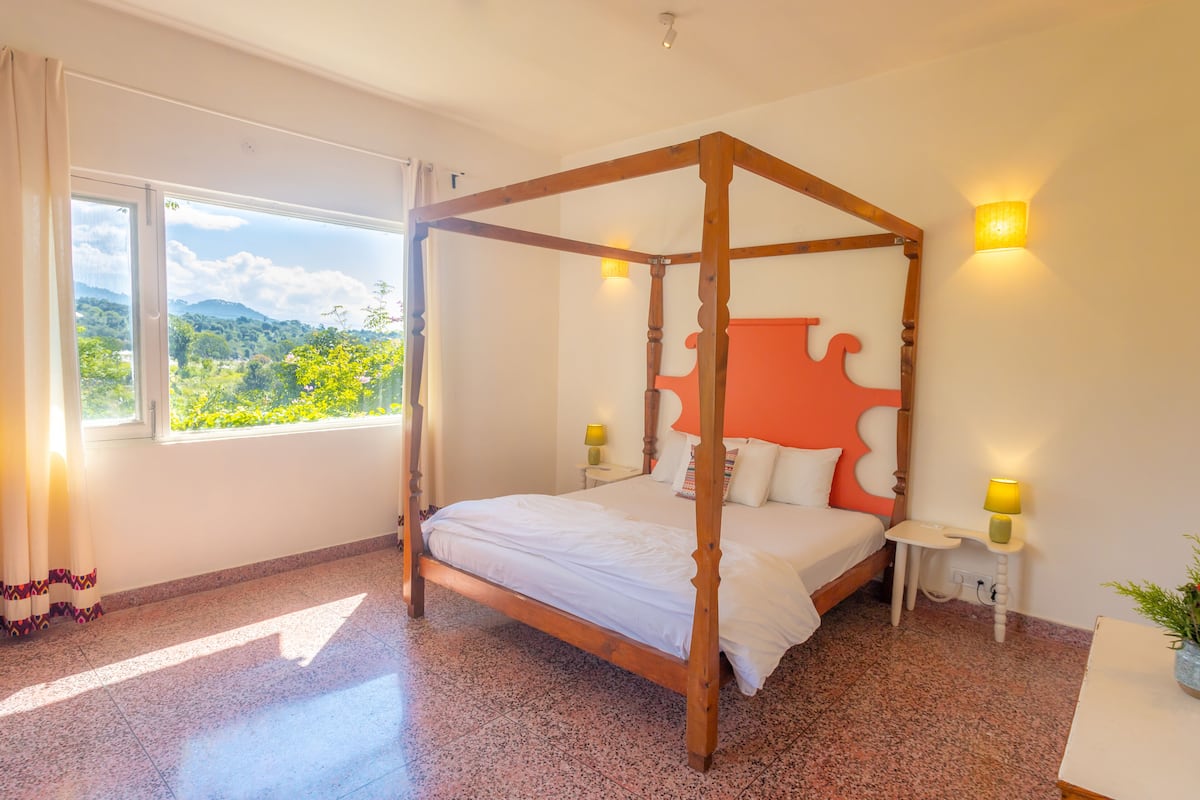 Una cama con dosel con vistas a un paisaje montañoso a través de un amplio ventanal.