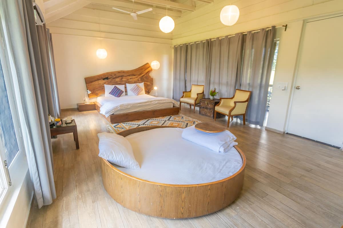 Un dormitorio amplio con una cama redonda grande, un cabecero de madera, una mesita de noche pequeña, una silla y un ventanal con cortinas.