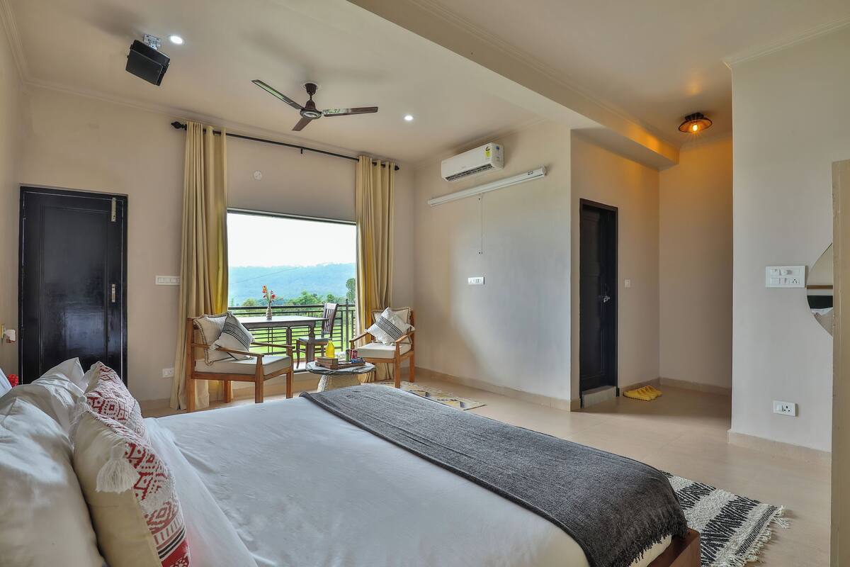 Una habitación de hotel con una cama grande, un balcón con vistas, un ventilador de techo y aire acondicionado.