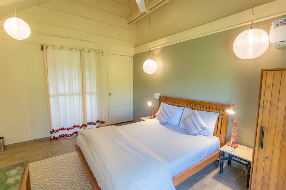 Un dormitorio con una cama grande, una mesita de noche con lámpara, un armario y una ventana con cortinas.