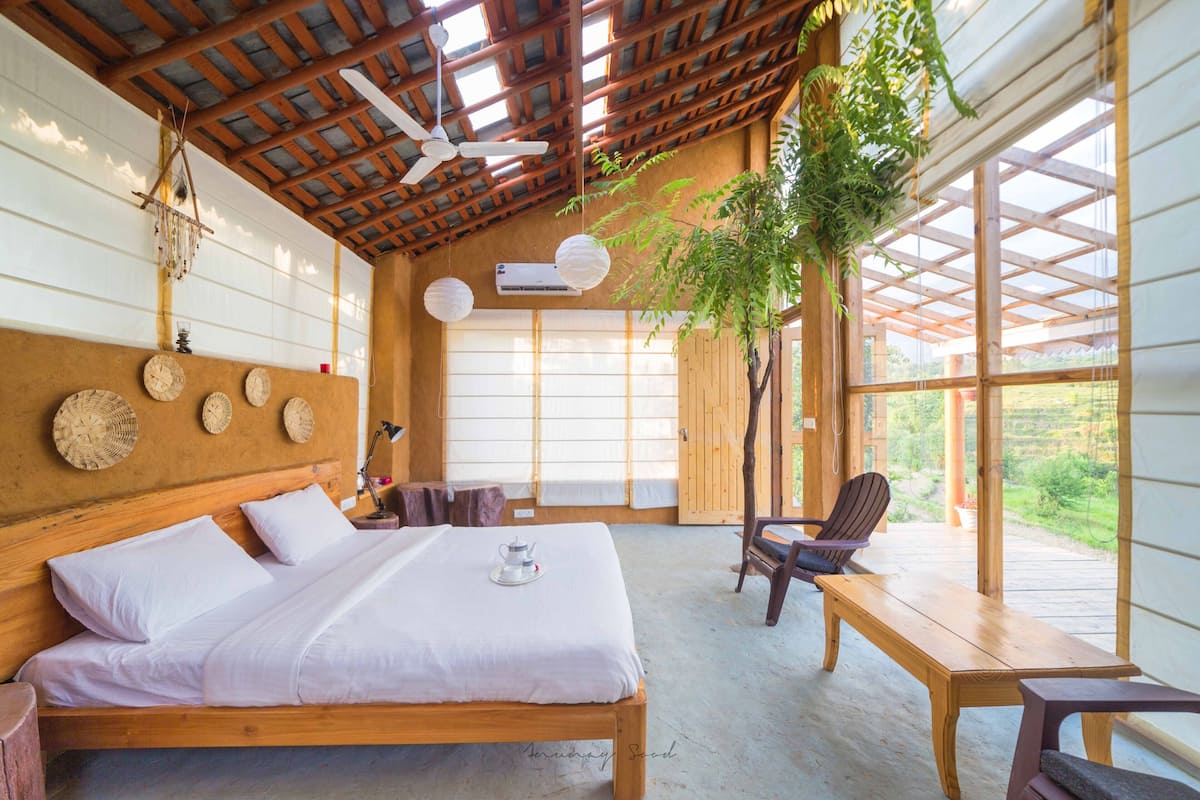 Una habitación con una cama de madera, una mesa, sillas y vistas al verdor exterior.