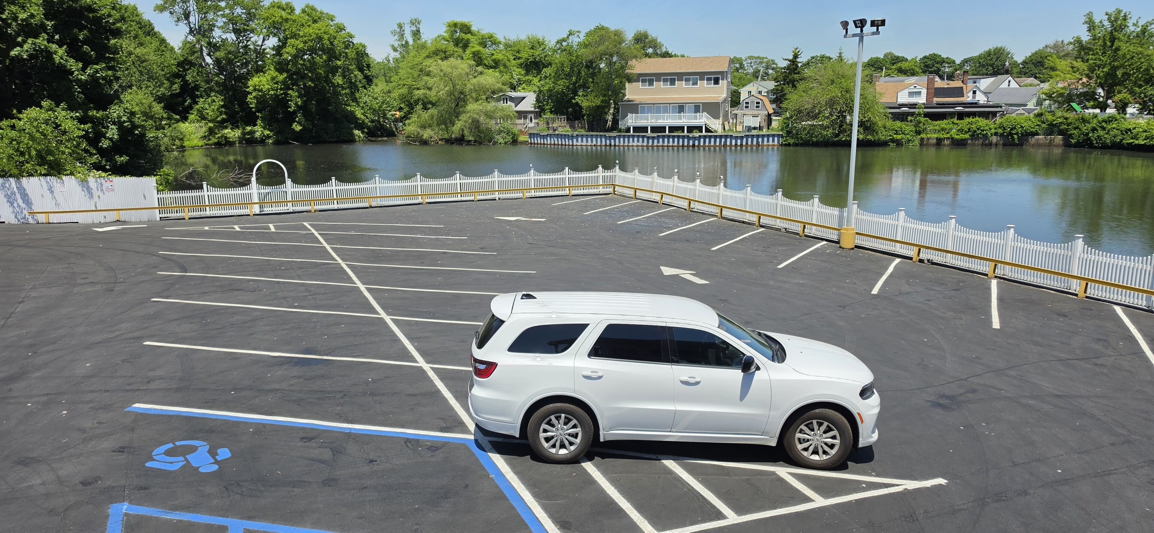 A parking lot with a white SUV, marked spaces, and a white fence.