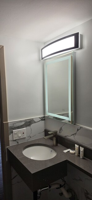 A modern bathroom with a marble vanity, a large mirror with integrated lighting, and a visible electrical outlet.