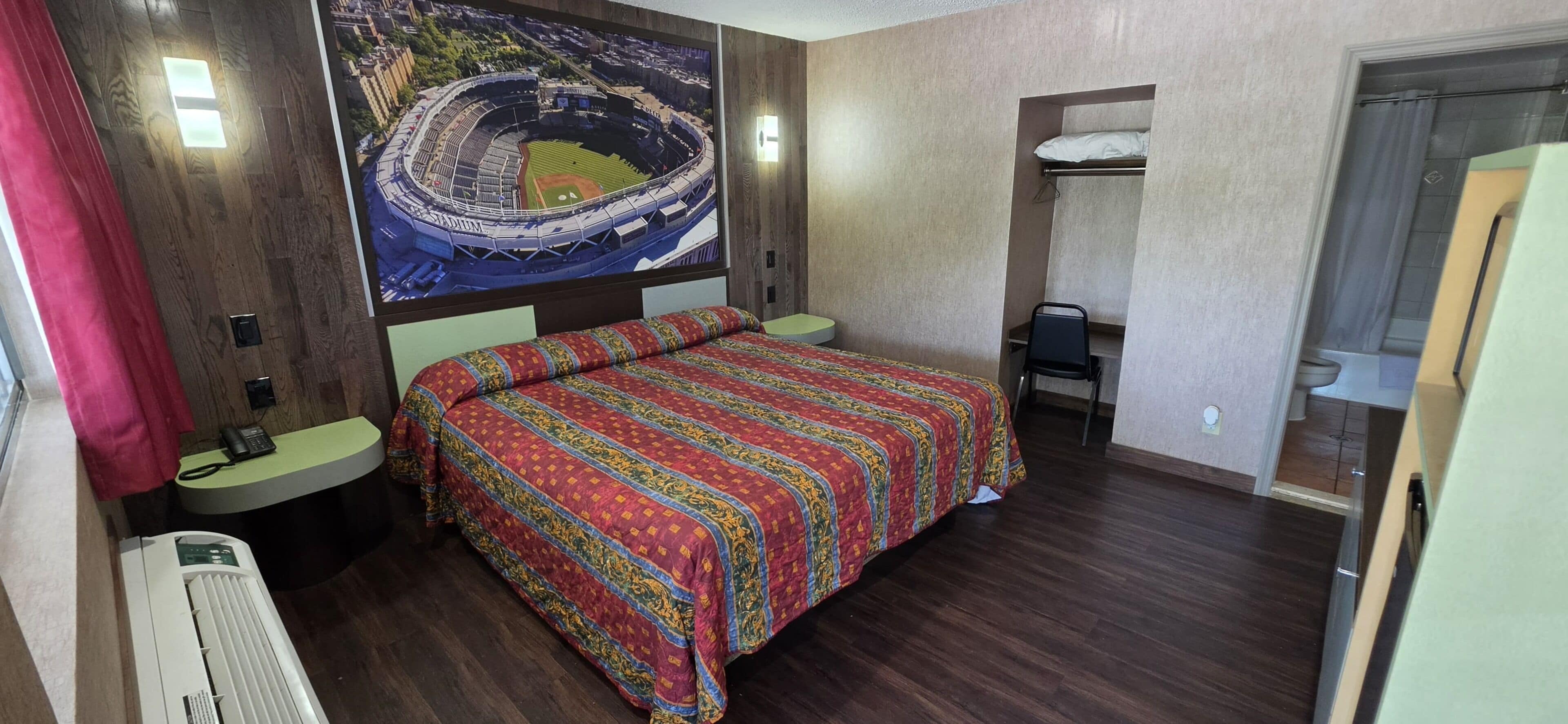 A hotel room with a bed, a desk, a chair, a telephone, and a large wall mural.
