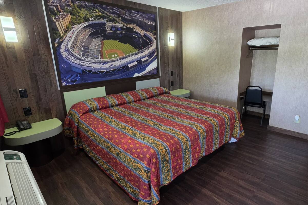 A hotel room with a bed, a desk, a chair, a telephone, and a large wall mural.