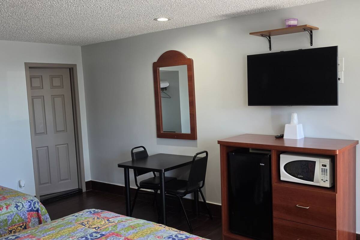 A hotel room with a bed, a desk with a chair, a microwave, a television, a mirror, and a door.