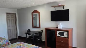 A hotel room with a bed, a desk with a chair, a microwave, a television, a mirror, and a door.