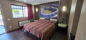 Ein Hotelzimmer mit einem großen Bett, einem Fenster mit Ausblick, einer Wand-Klimaanlage und einem Poster eines Stadions.