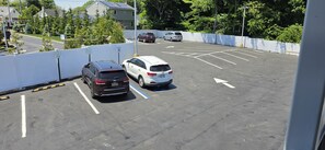 A parking lot with marked spaces, a white fence, and a building in the background. - South Bay Motel (Copiague)