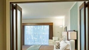 A hotel room with a large bathtub, a bed with a blue blanket, and a nightstand with a lamp. - Manoir du Lac William (St-Ferdinand)