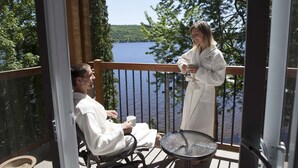 A balcony with a view of a lake, a table, and two people in bathrobes. - Manoir du Lac William (St-Ferdinand)