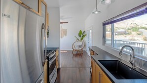 A modern kitchen with stainless steel appliances, wooden cabinets, and a large window offering a view of the outdoors.
