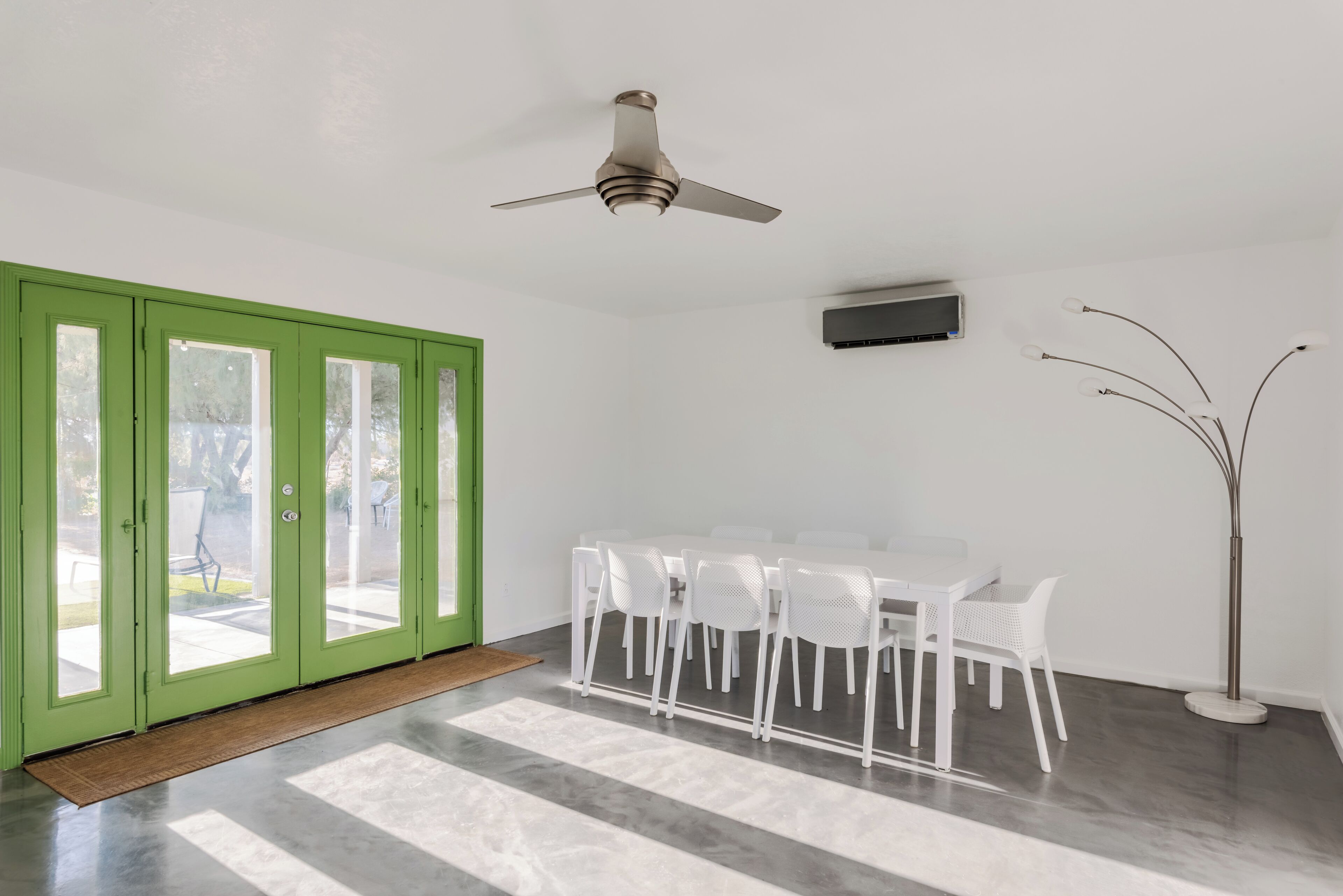 Un'area pranzo moderna con una ventola a soffitto, un tavolo bianco con sedie e una porta verde che dà sull'esterno.