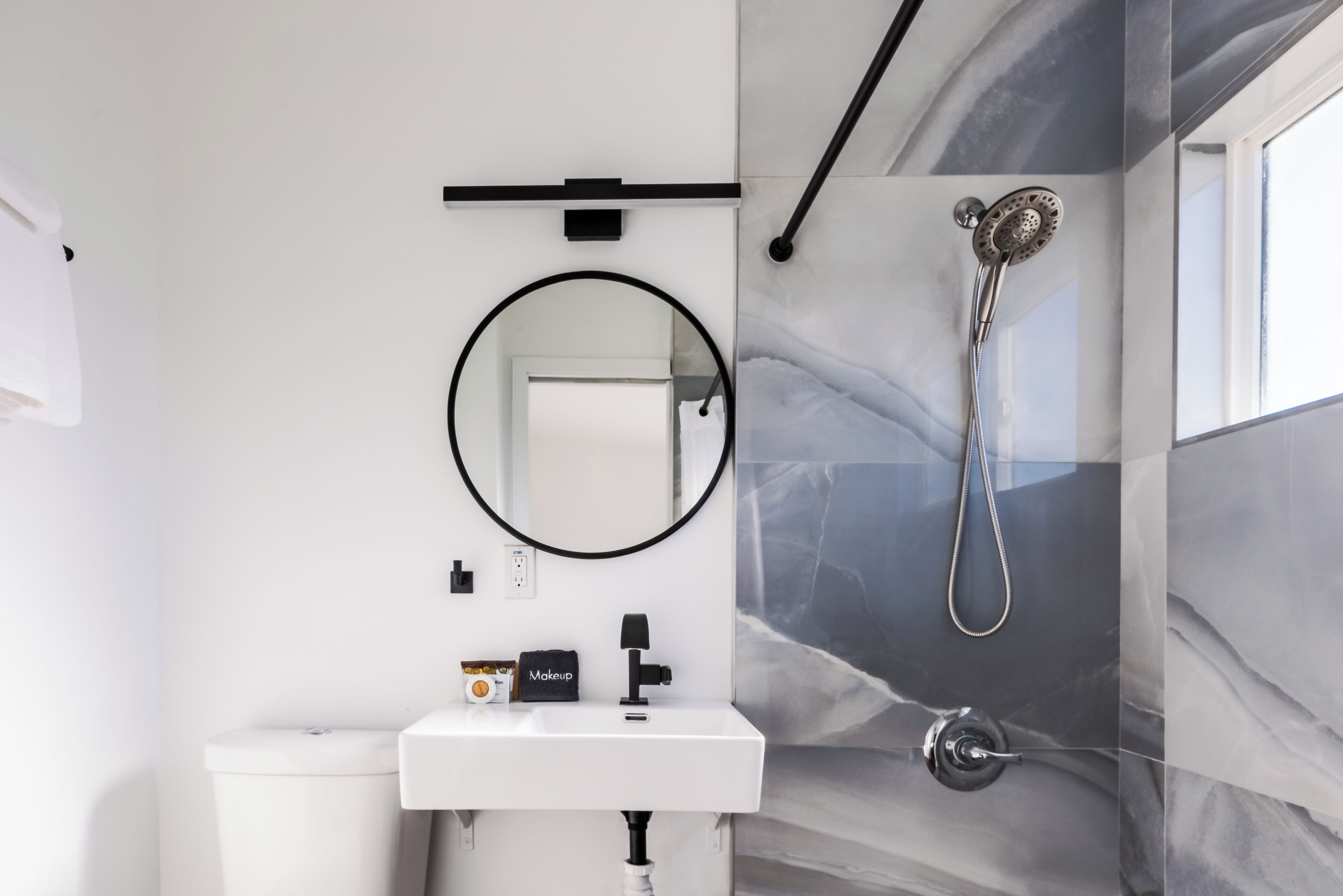 Une salle de bain moderne avec un lavabo blanc, un miroir rond, une douchette à main et des murs à motifs de marbre.
