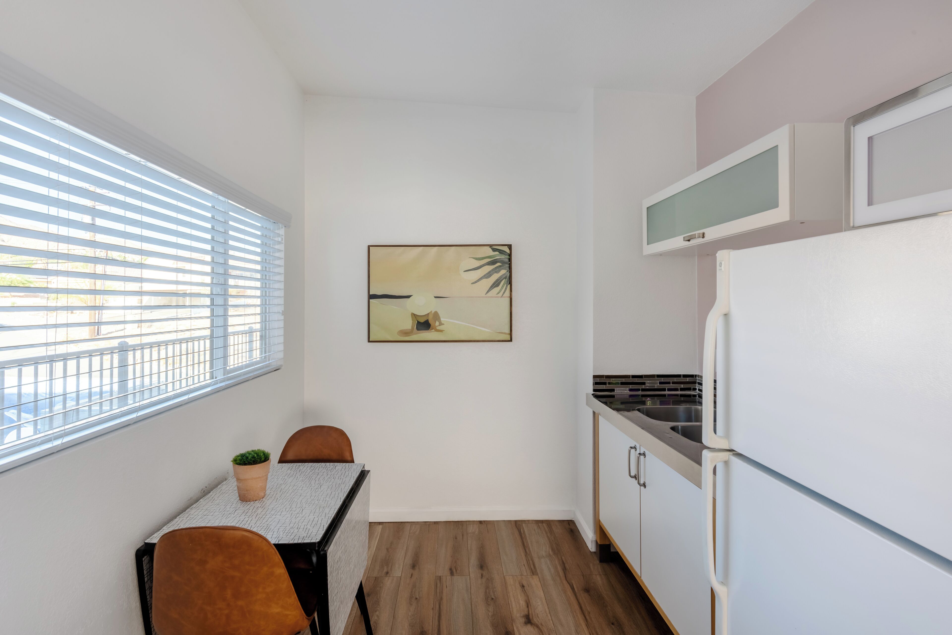 A compact kitchen with a dining table, chairs, a refrigerator, and a microwave.
