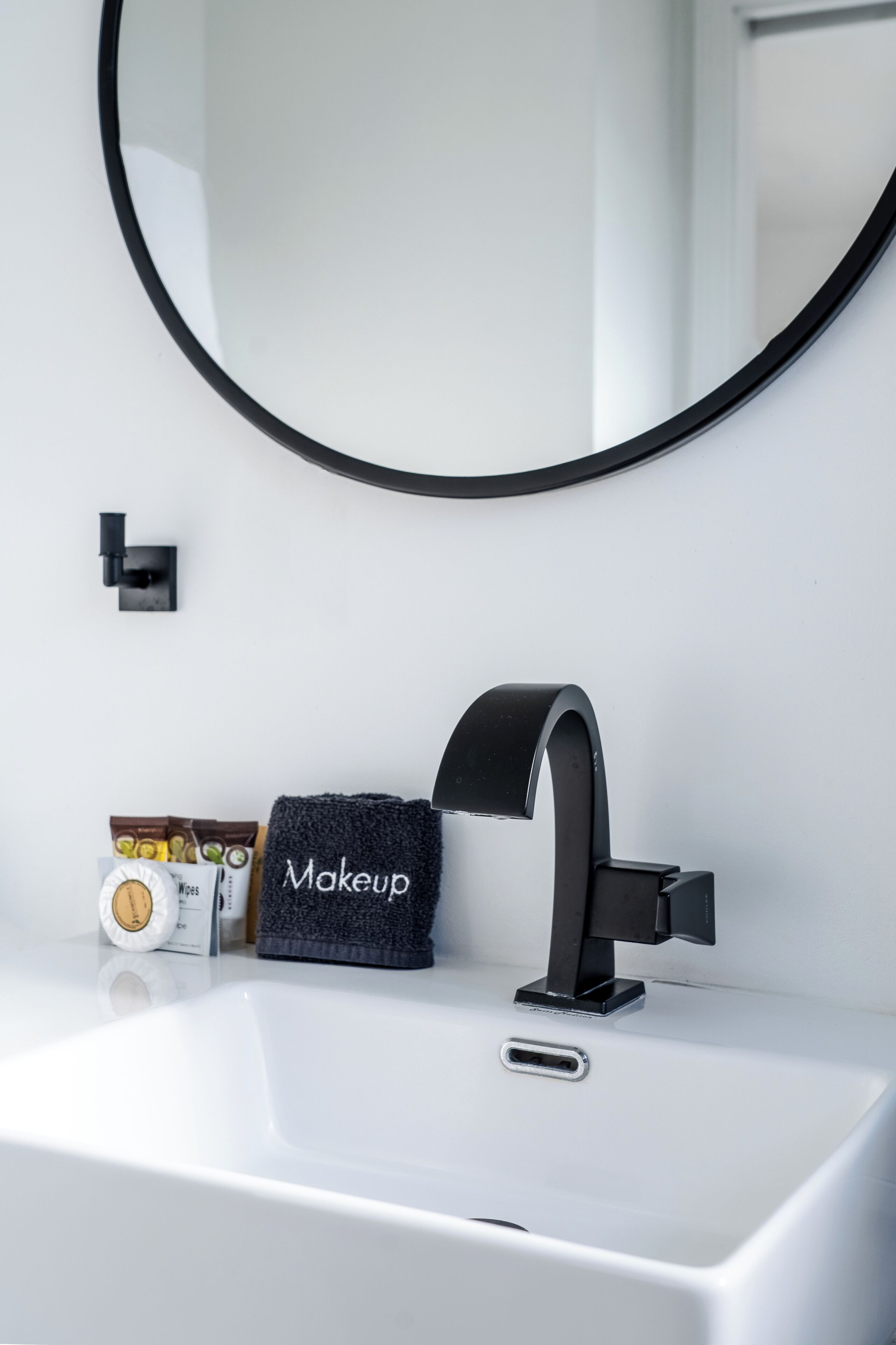A modern bathroom with a white sink, a black faucet, and a towel labeled "Makeup" on the counter.