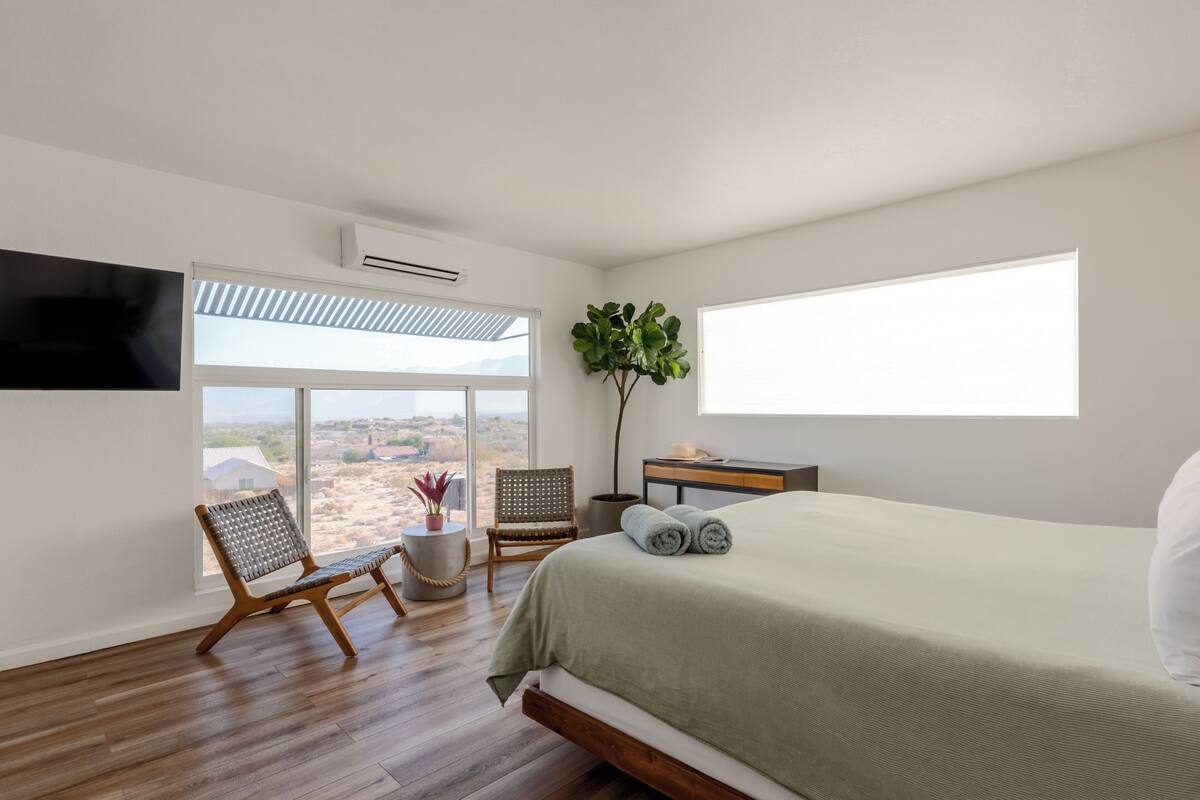 A bedroom with a large bed, a chair, a small table, and a potted plant.