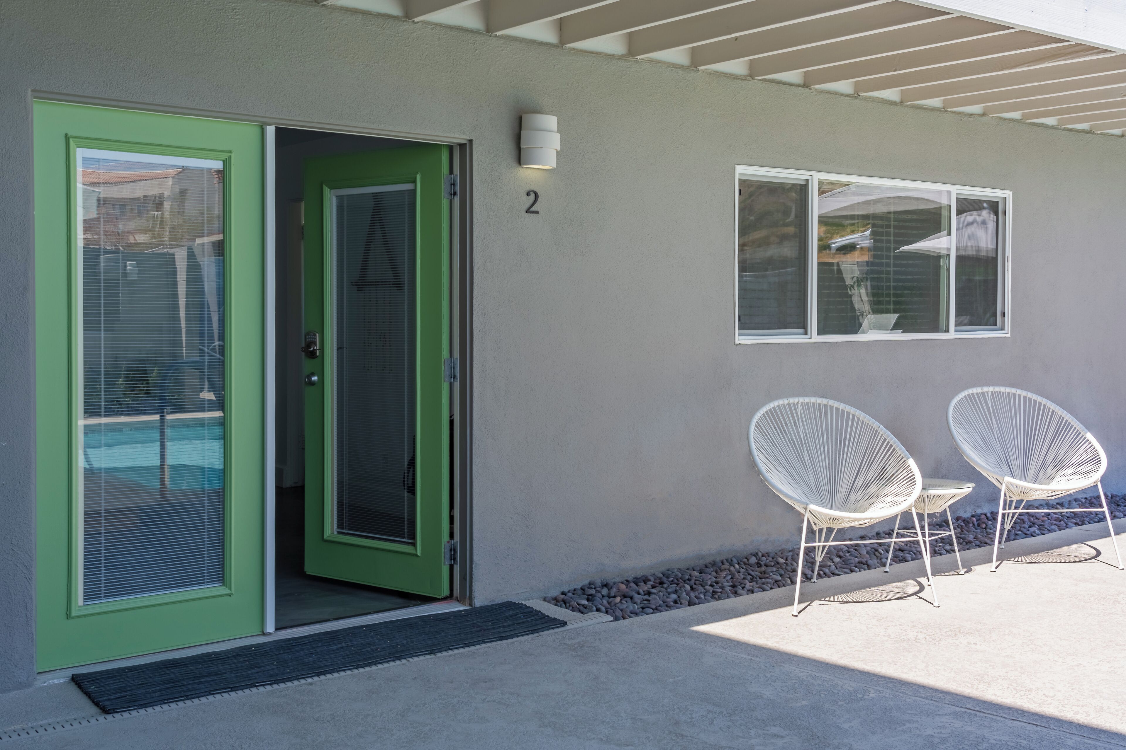 A building entrance with a green door, a number '2' sign, and two white chairs outside.