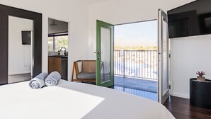 A modern bedroom with a large bed, a green door leading to a balcony, and a view of a desert landscape.